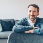 Smiling man sitting on a couch in a clean, modern living room, suggesting comfort and fresh indoor air