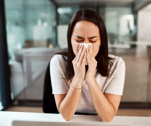 A picture of a woman with a kleenex trying to blow her nose
